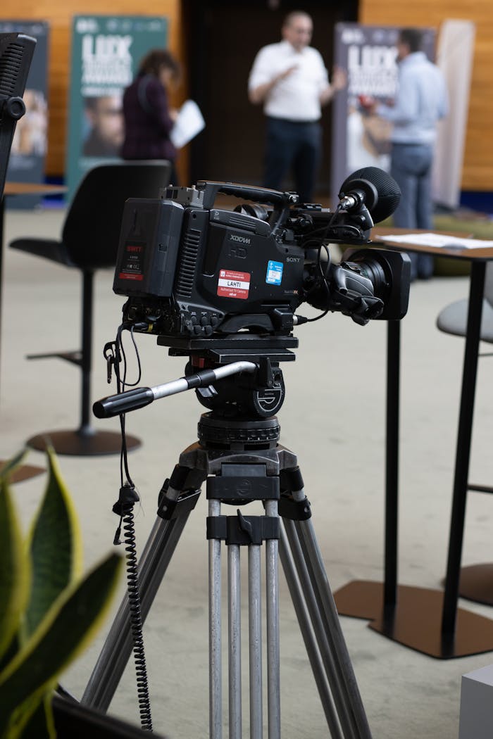 A video camera on a tripod in a modern office setting with people in the background at Strasbourg event.