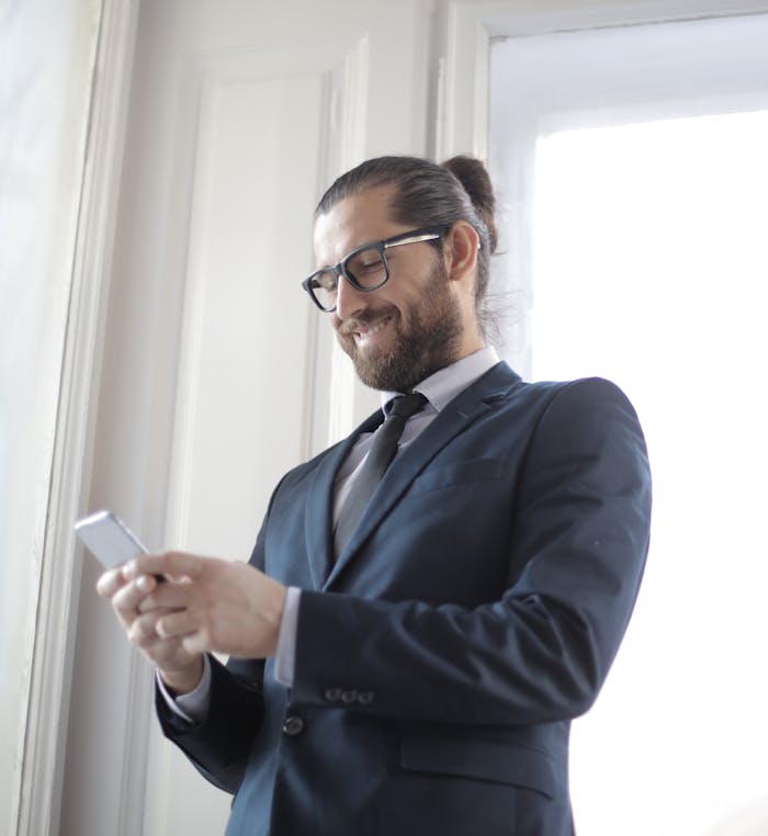 A confident businessman with glasses using a smartphone indoors, embodying success.