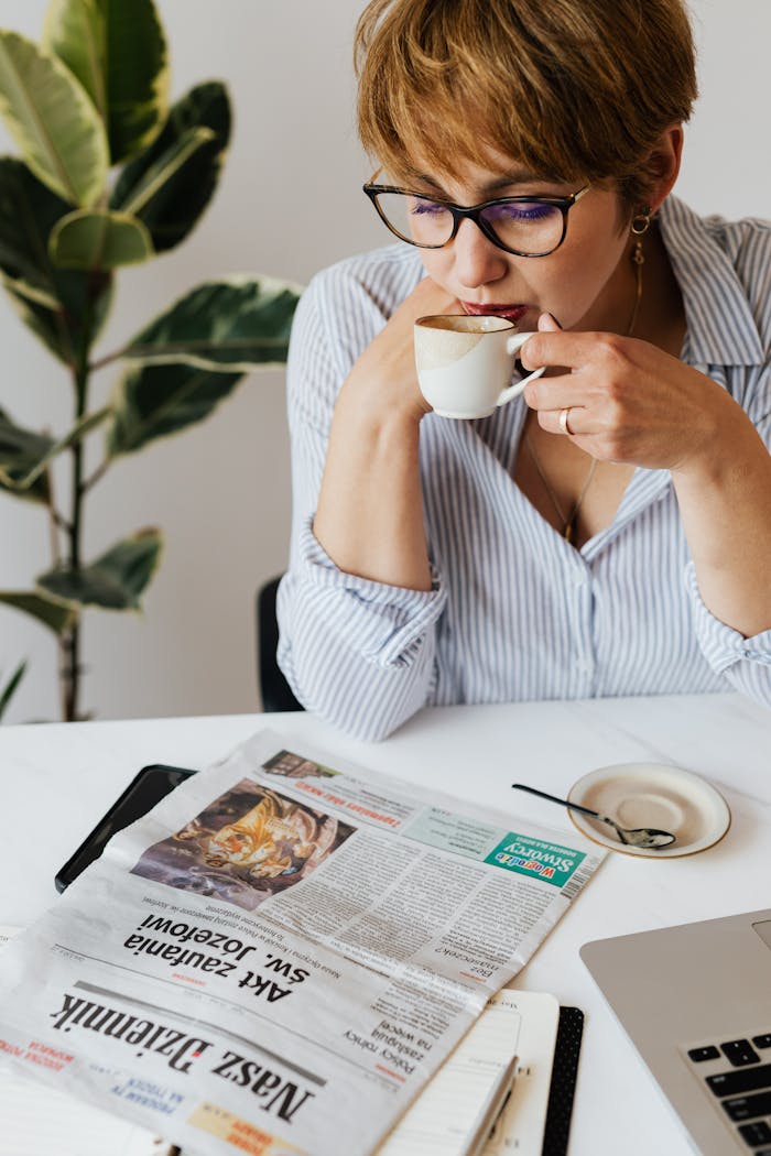 Woman enjoys a coffee break with a newspaper at her workspace, creating a modern and intellectual vibe.